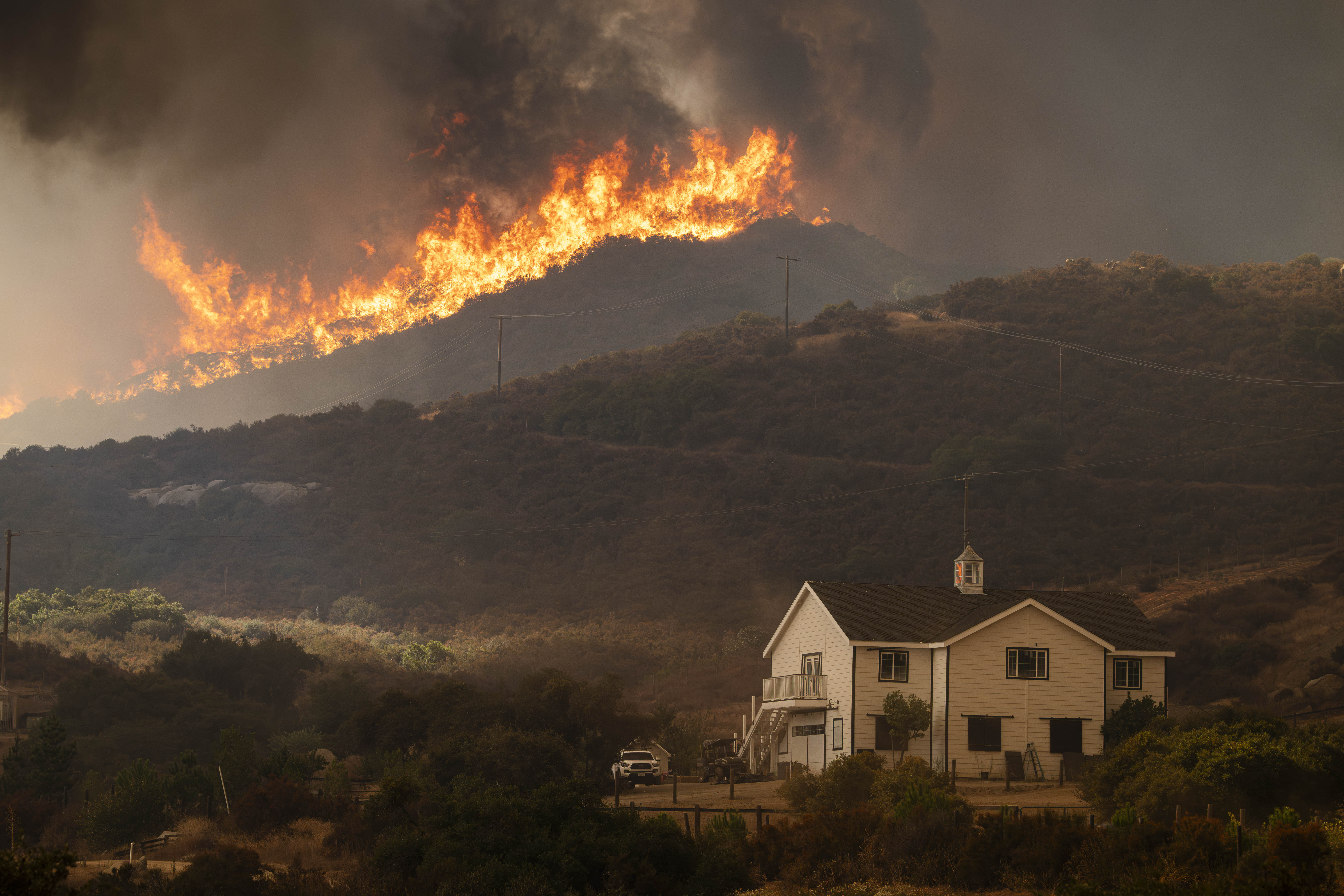 House sitting at the bottom of a hill that is on fire.