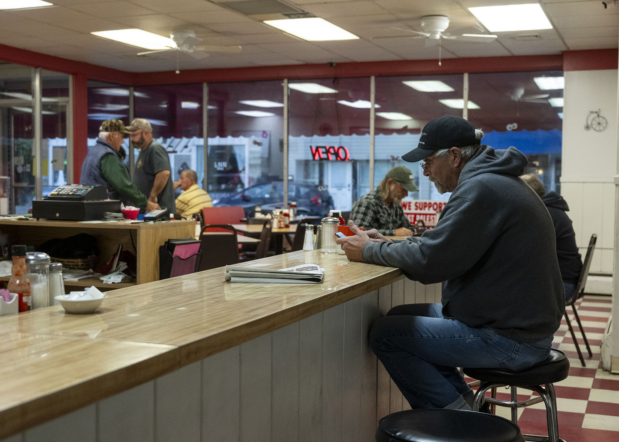 A man sits at a diner counter, looking at his phone.