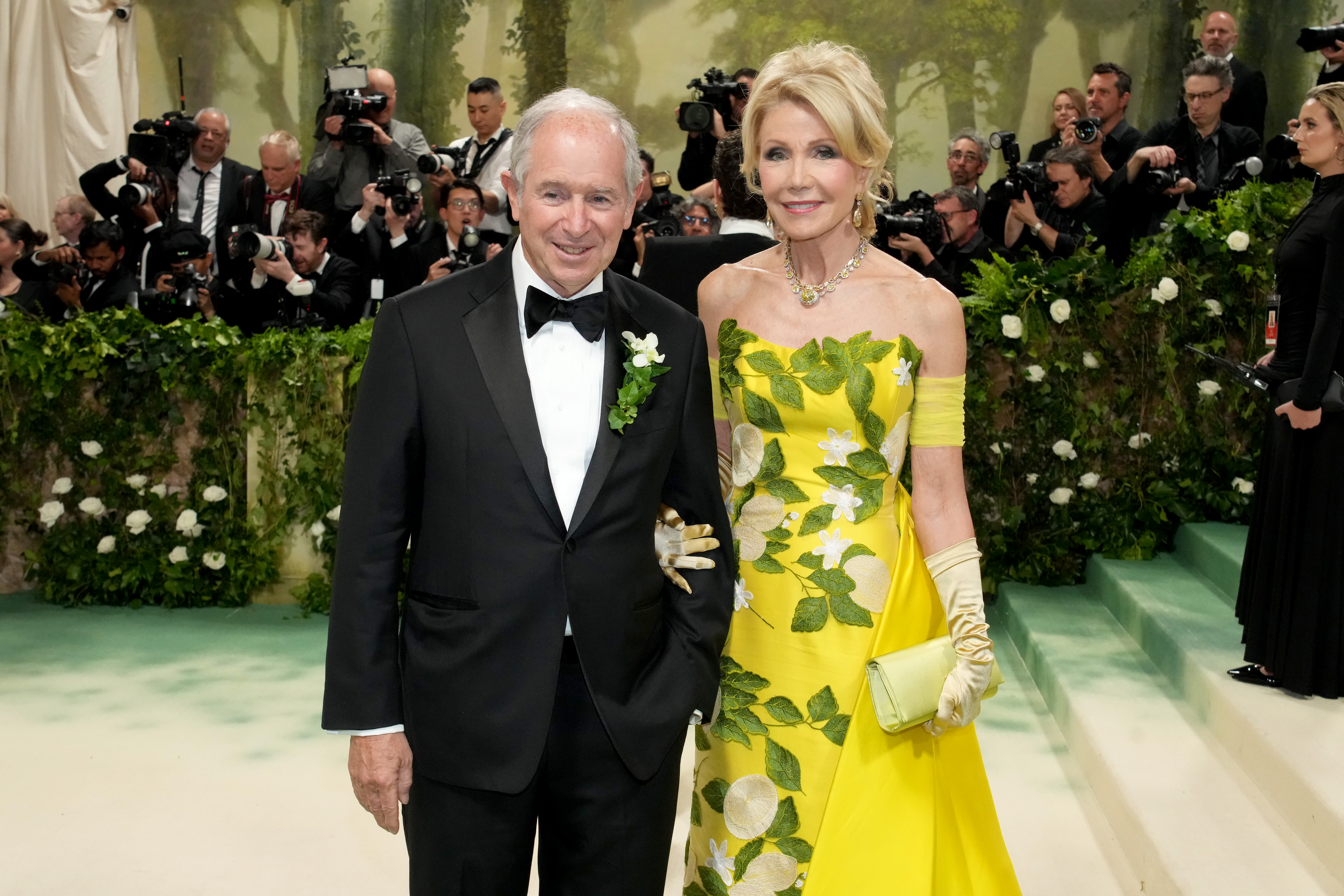 Man in a tuxedo and woman in a yellow dress stand, posing for a photo.