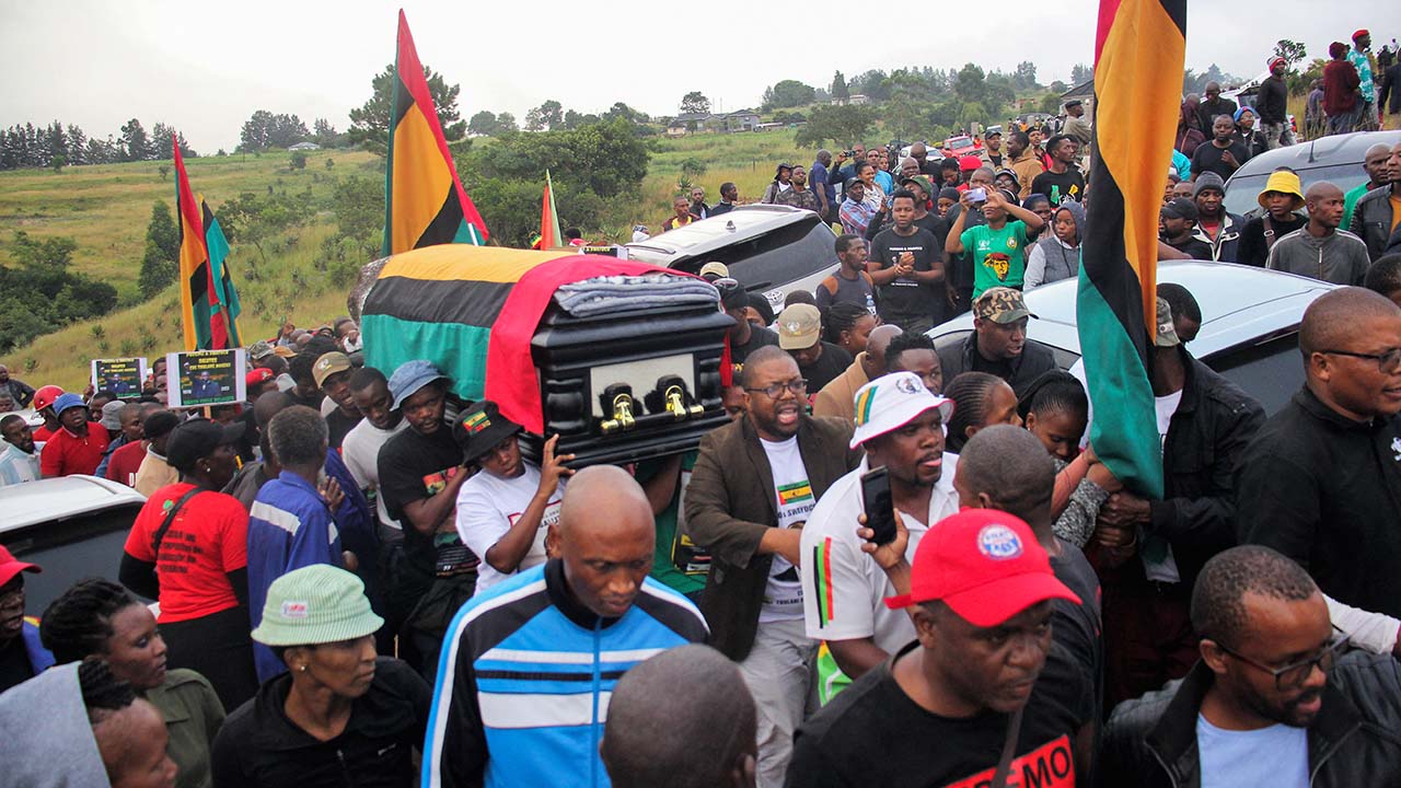 Photo of a large crowd waving flags, with a flag-draped coffin being carried through its midst.