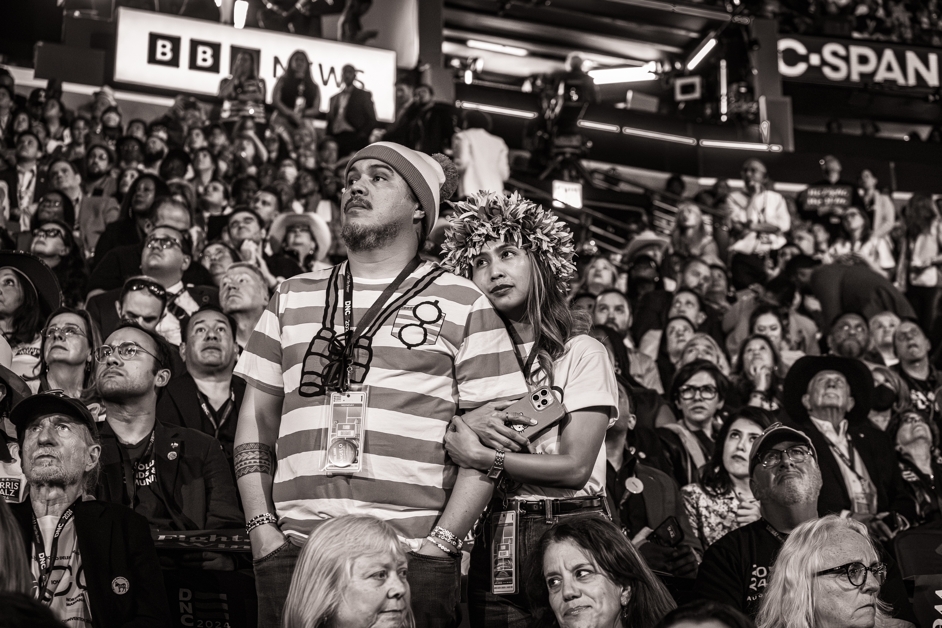 Black and white photo of a man and woman hugging among a crowd of people. The man is dressed like Waldo from the "Where's Waldo?" books.