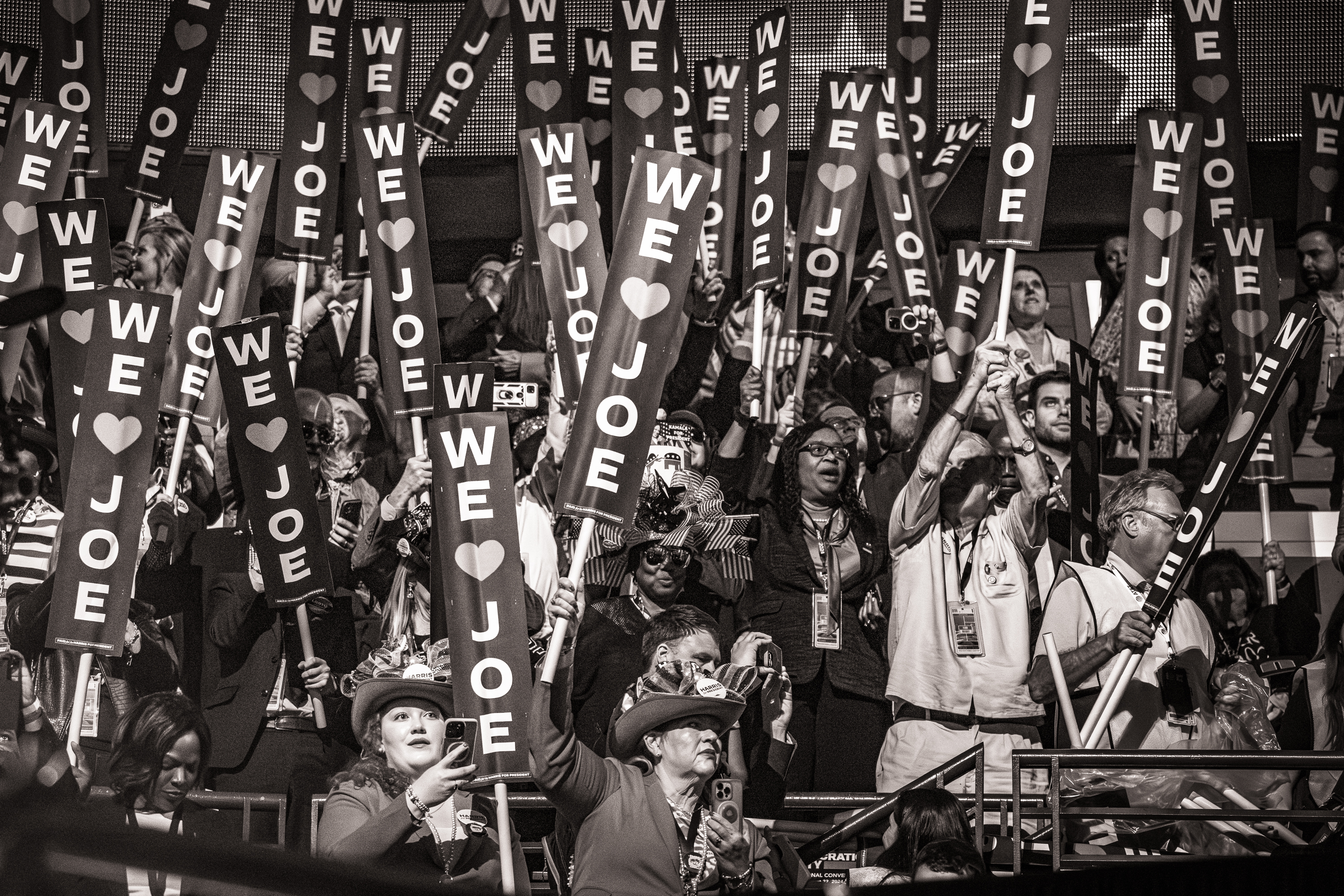 Black and white photo of a crowd of people waving We Love Joe signs.