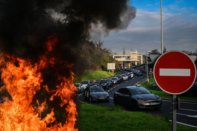 A fire is seen as taxi drivers block the roads during a demonstration against a new downward pricing system for medical transport and a "shared taxi" obligation proposed by the Caisse Nationale d'Assurance Maladie (CNAM), in Lyon central-eastern France on December 2, 2024. Several hundred taxi drivers began slowing down or blocking several access points to the Lyon metropolitan area on December 2, 2024 morning, to protest against the agreement being negotiated with the French health insurance scheme for the transport of seated patients, according to the Rhone prefecture.