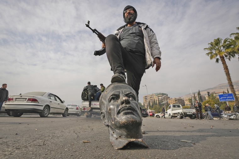 An opposition fighter steps on a broken bust of the late Syrian President Hafez Assad