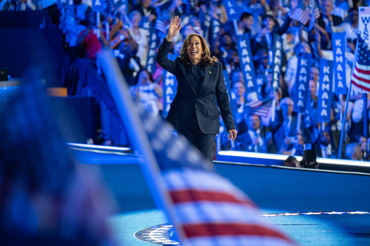 Kamala Harris walks and waves on stage while smiling