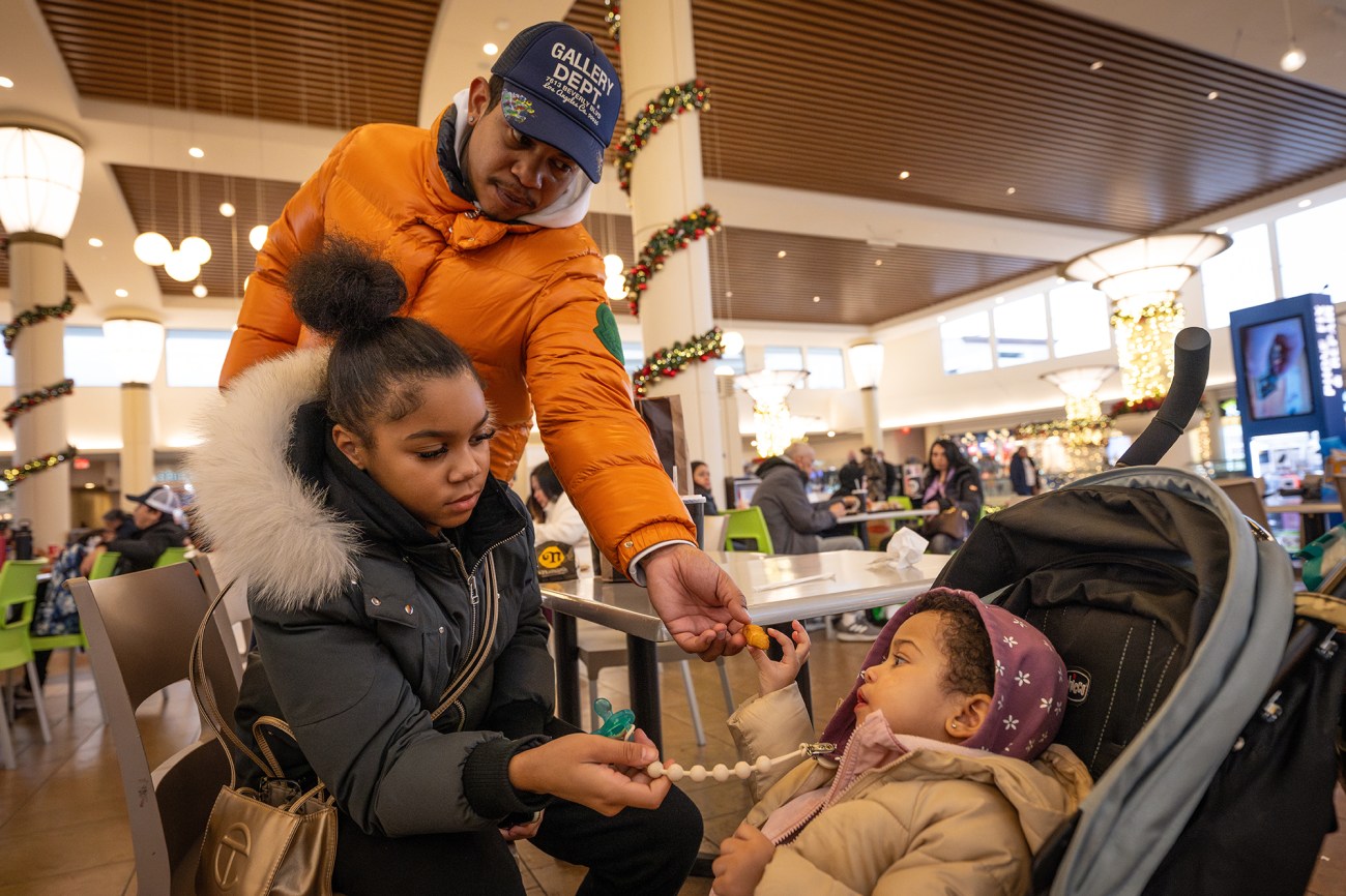 A man and a young girl playing with a child in a stroller at a mall.