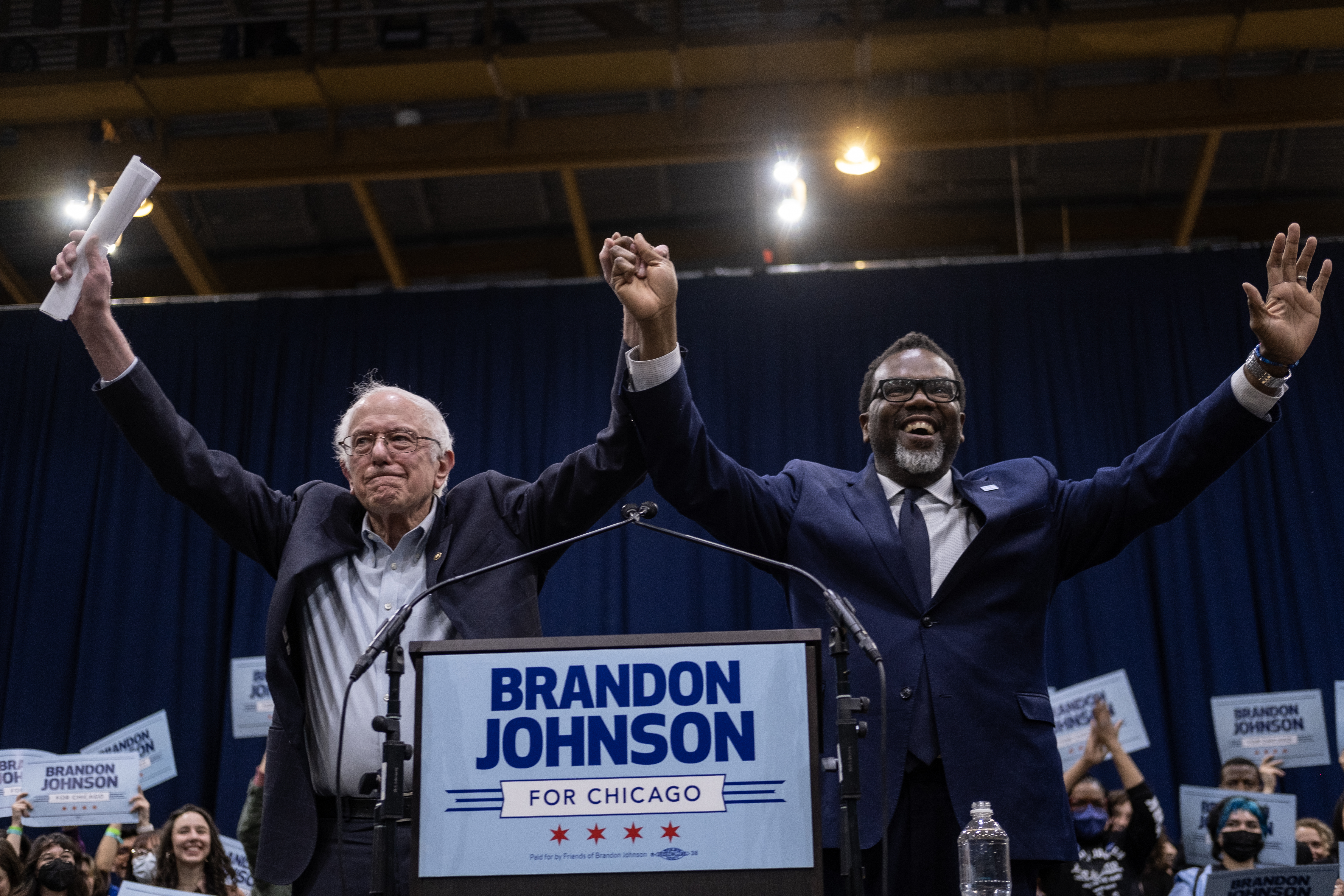 Brandon Johnson and Bernie Sanders raise their hands to a crowd of supporters