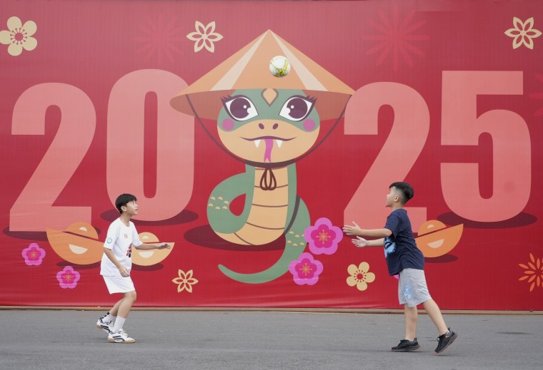 Two boys play football in front of a billboard welcoming the New Year 2025