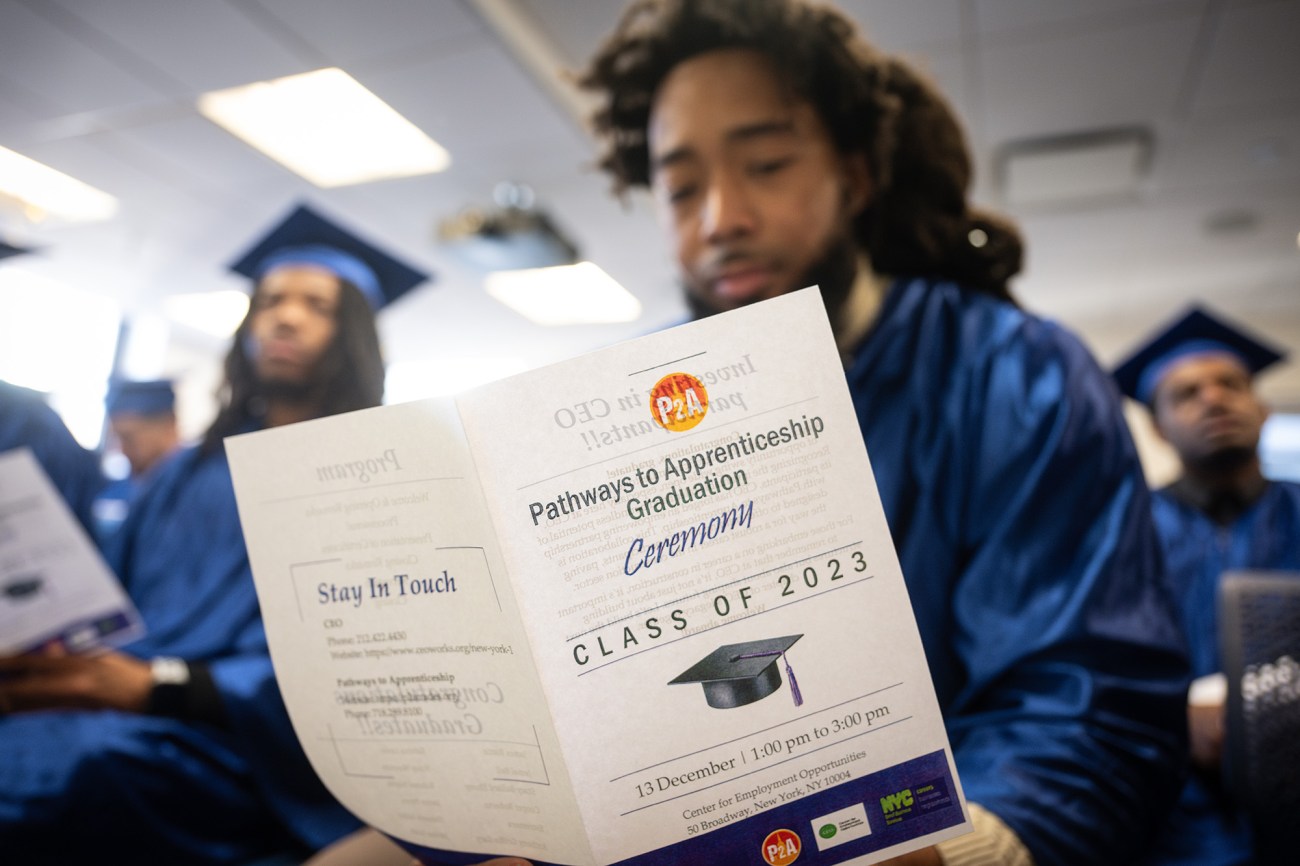 A man reading a pamphlet that reads, "Pathways to Apprenticeship Graduation Ceremony."