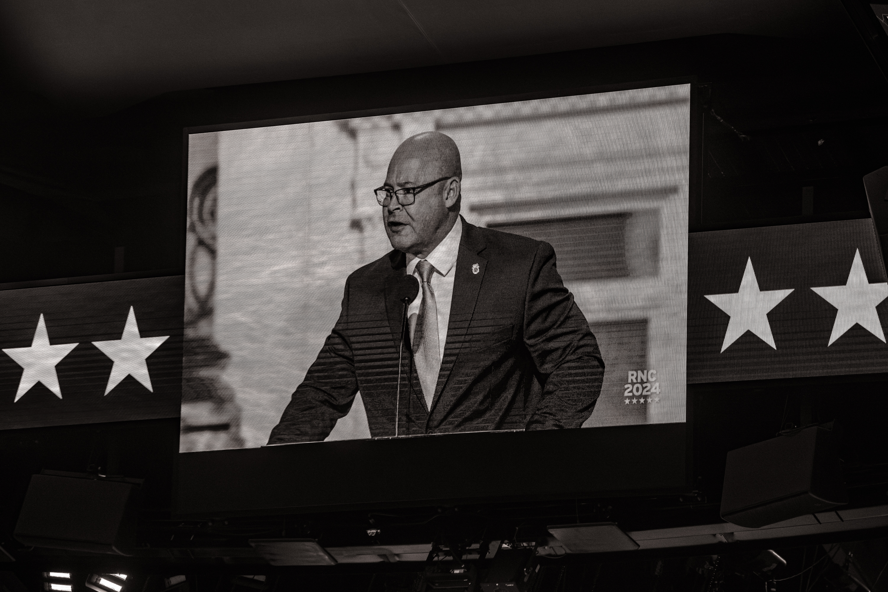 Sean O'Brien shown on a giant screen speaking. Two stars on either side of the screen.