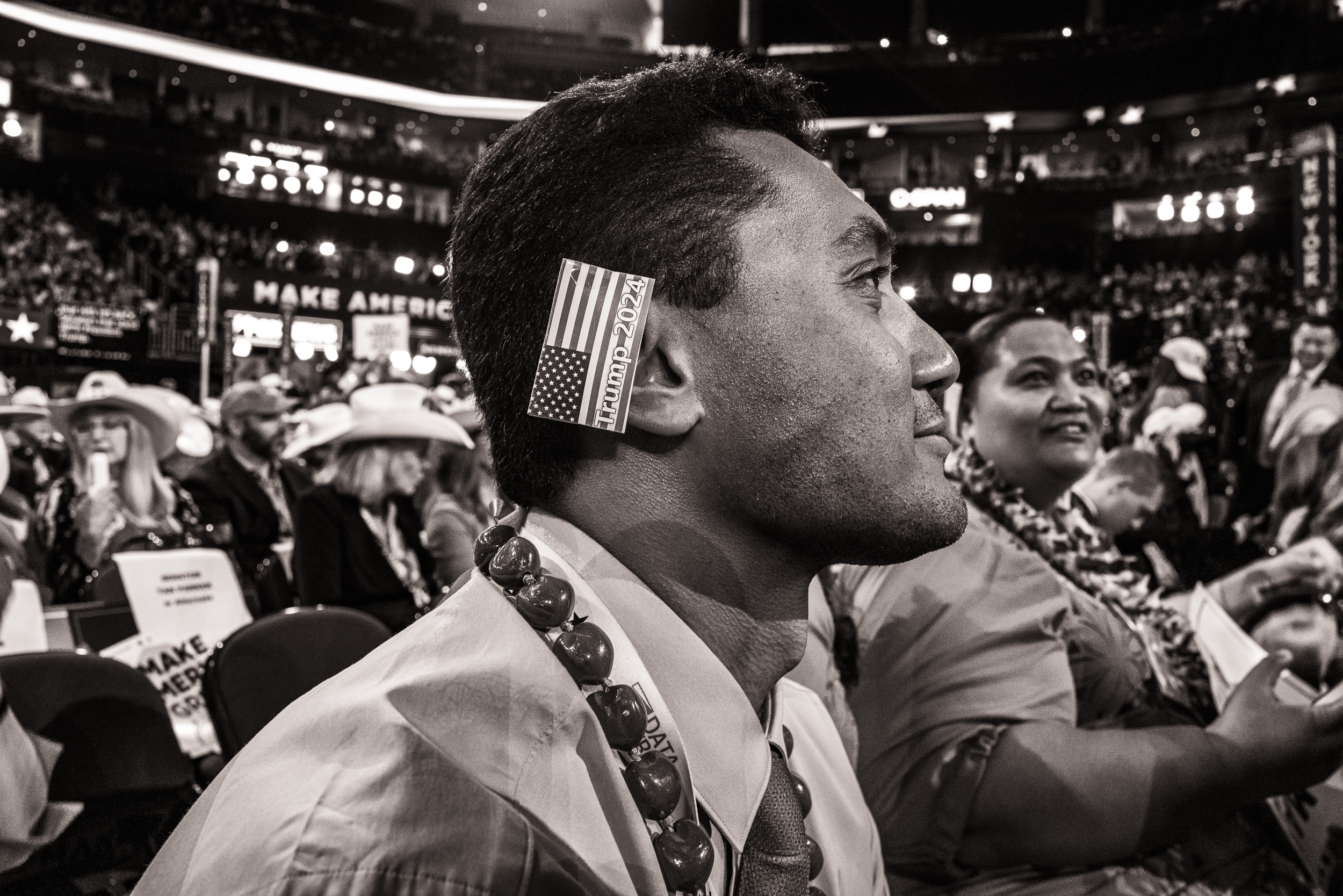 Black-and-white photo of man with an American flag ear "bandage" that reads, "Trump 2024."