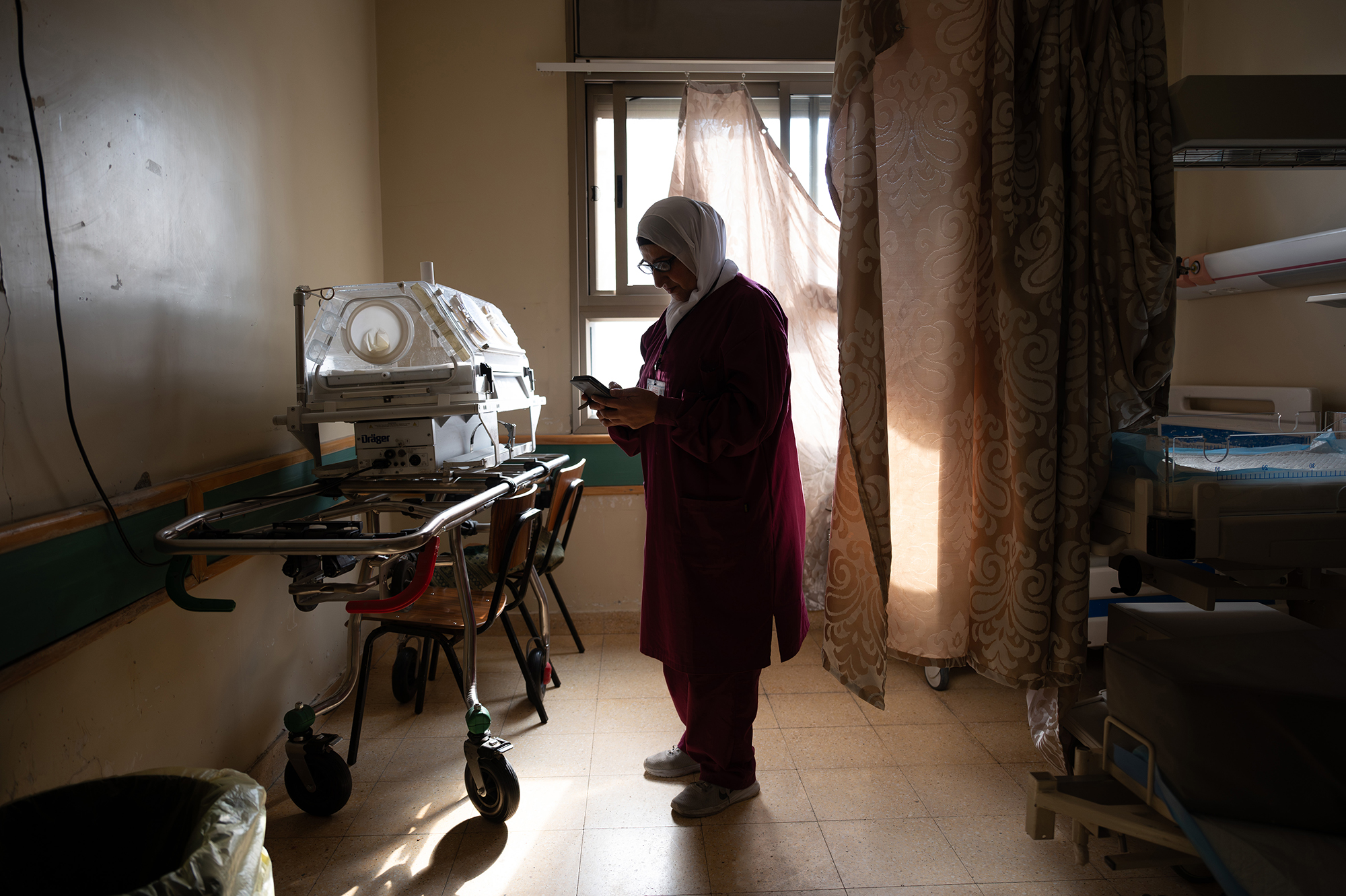 A woman standing amid hospital equipment, texting on her phone.