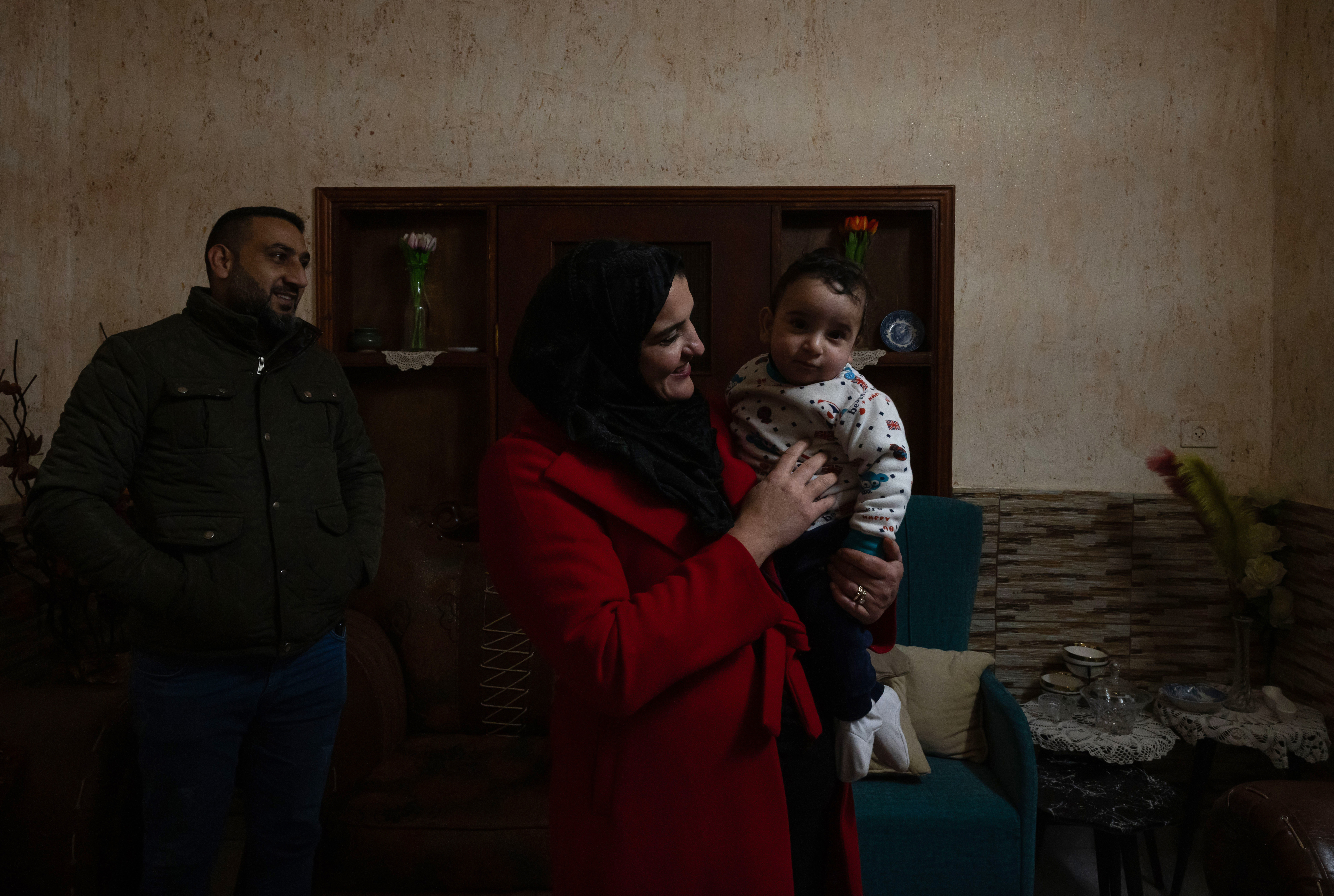 A woman holds a baby, smiling. A man looks on behind her.