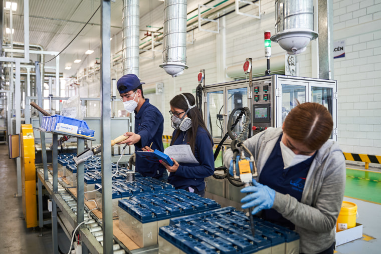 Workers wearing masks weld acid batteries in a factory