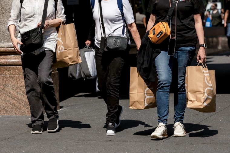 Shoppers carry Macy's bags while walking on the sidewalk