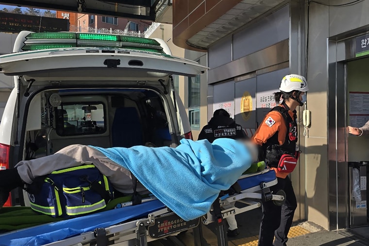 A passenger (face digitally blurred) is transferred from an ambulance to a medical facility