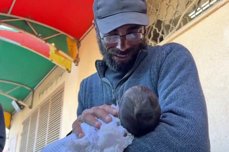 Yahya Al-Batran holds the motionless body of his newborn baby, Jumaa, wrapped up in a blanket.