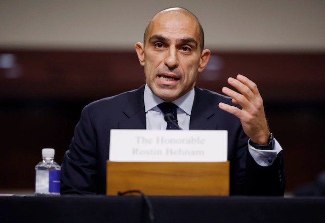 Rostin Behnam, a bald man with light brown skin, speaking from a table