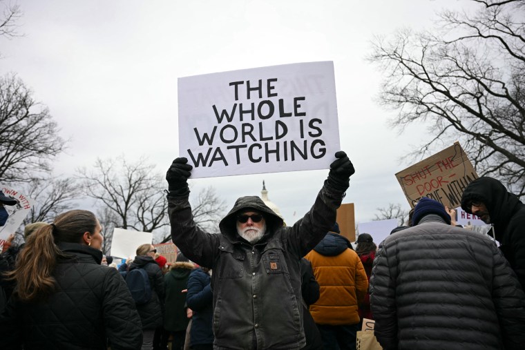 A man holds a sign saying "The whole world is watching"