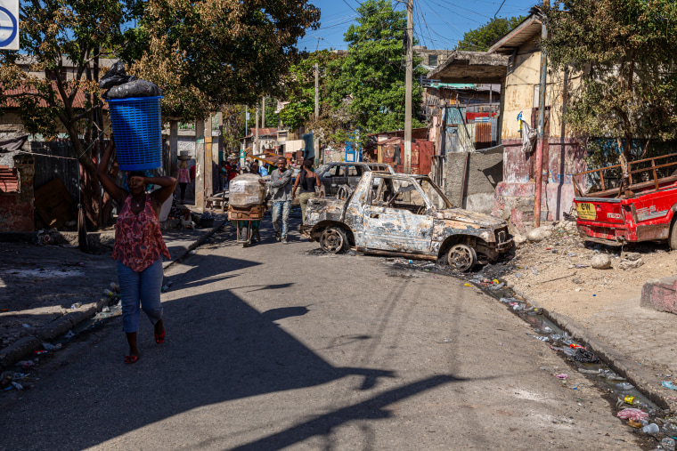 People walk past a car set on fire.